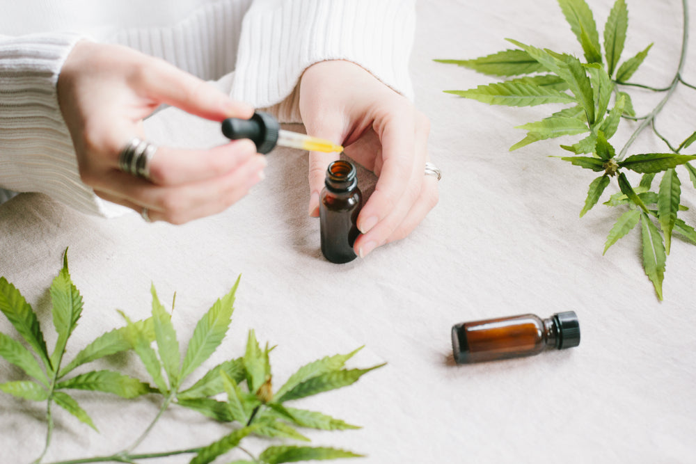 A woman holds homemade THC oil in a tincture surrounded by cannabis leaves.