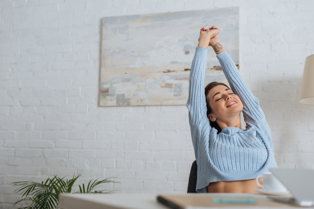 A woman happily stretches at her desk 